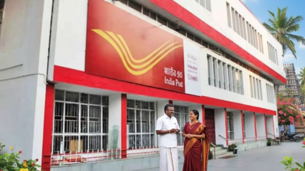 A high-resolution image of a modern white and red India Post building in a Tamil Nadu village. In the foreground, a man in a white dhoti and a woman in a maroon and gold saree (the post masters) stand smiling and talking near a colorful Kolam on the ground. The background shows lush greenery, a coconut tree, and the top of a traditional South Indian temple gopuram.